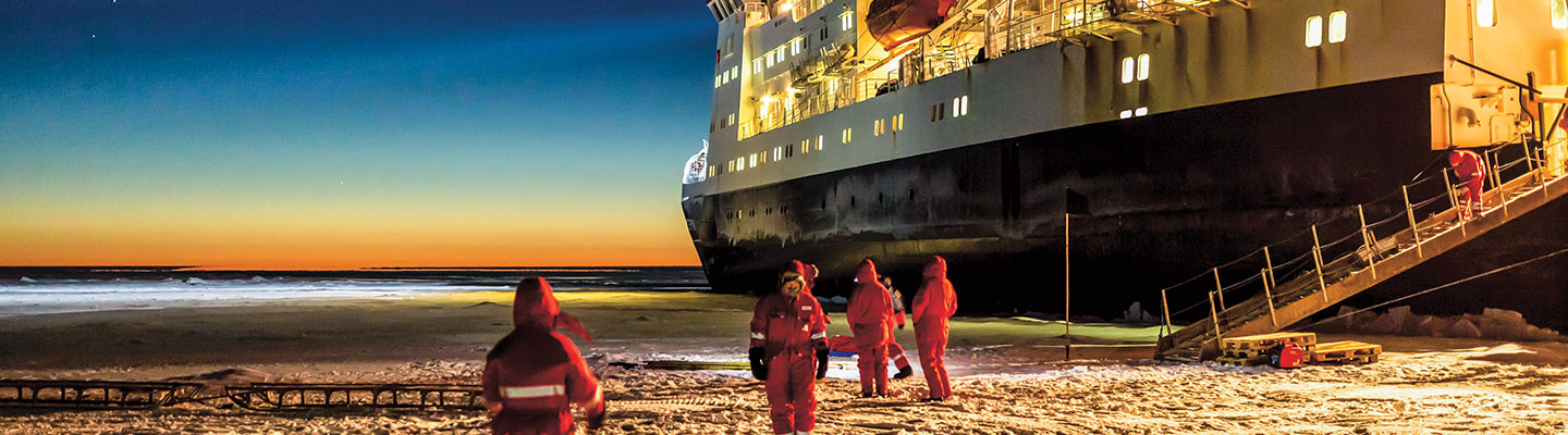 Scientists standing by a giant ship in Antarctica