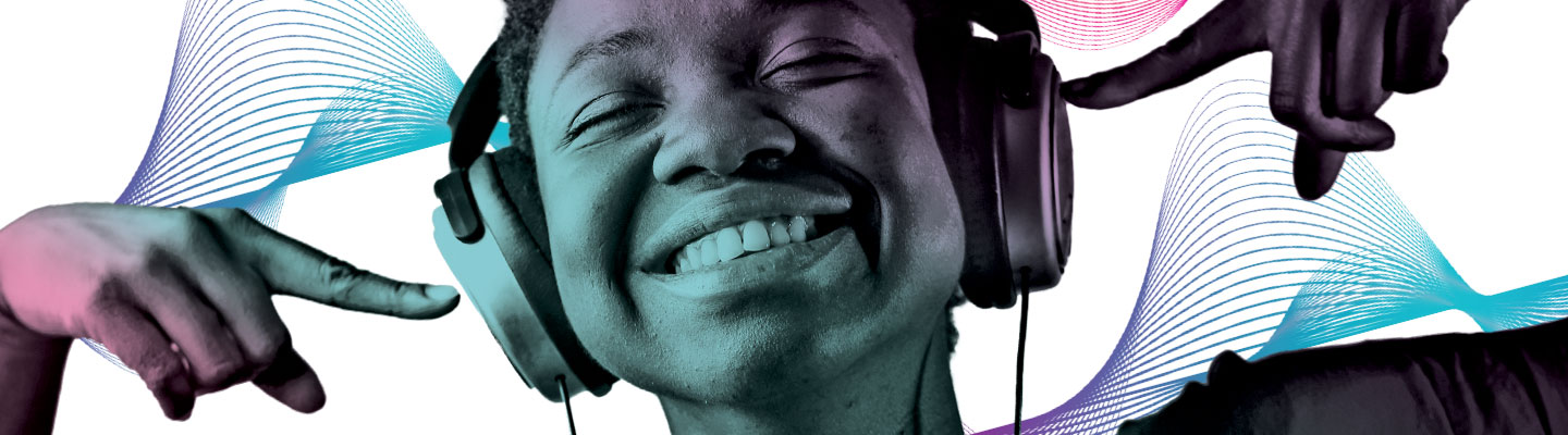 A boy wearing a pair of headphones and smiling while pointing to his ears