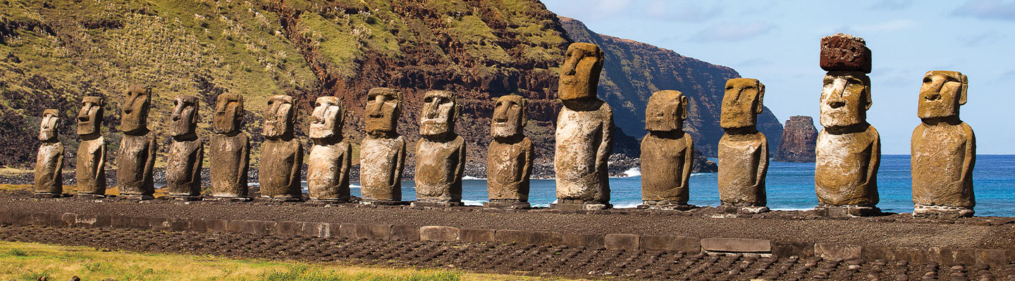 Row of moai statues on Easter Island with green hillside and ocean in background