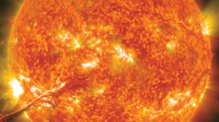 A close-up view of the sun with bright flares and a solar eruption along its surface