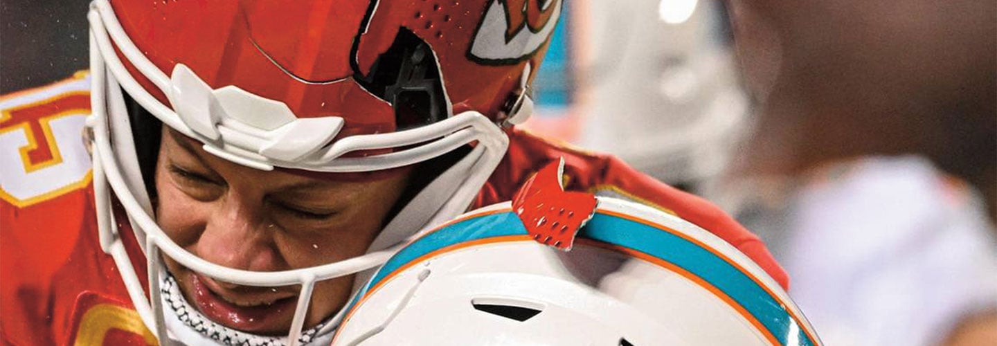 A football player in a red helmet grimaces as he collides with an opponent in a white teal helmet