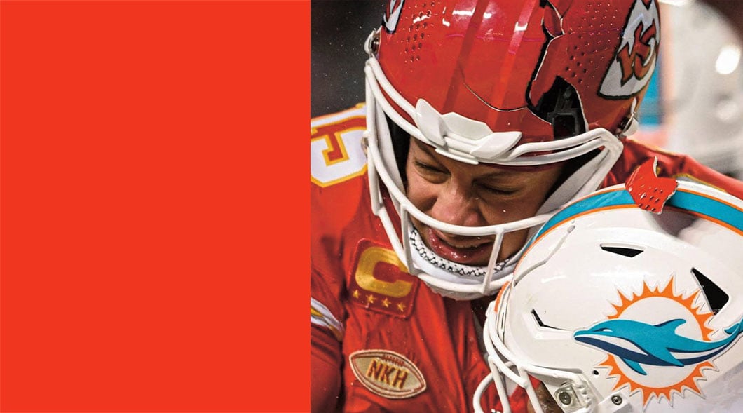 A Chiefs player in a red helmet grimaces as he leans his head against a Dolphins player's helmet
