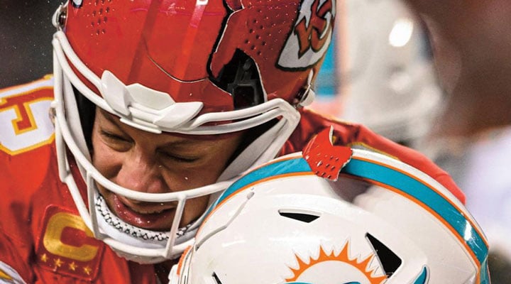 A Chiefs player shuts his eyes & leans his red helmet against a white Miami Dolphins helmet